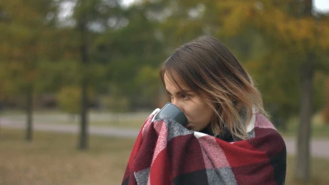 Girl in the autumn park.
Slow motion. A young girl is drinking a hot drink.