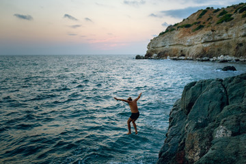 Man Jumping into the Ocean at Sunset, Summer Fun Lifestyle. Man jumping from the rock into the sea.