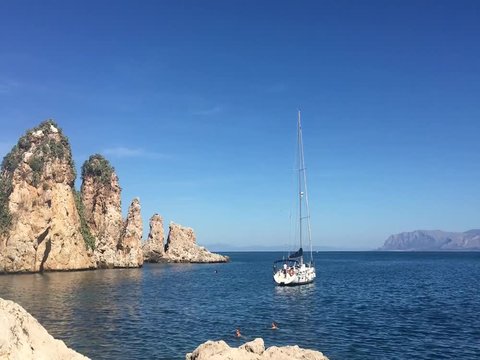 panoramic footage from scopello beach in sicily inside the zingaro national park with calm blue sea while a sailboat is moored off