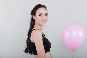 Fototapeta na wymiar Brunette girl in a black top, holding pink balloon on a light background