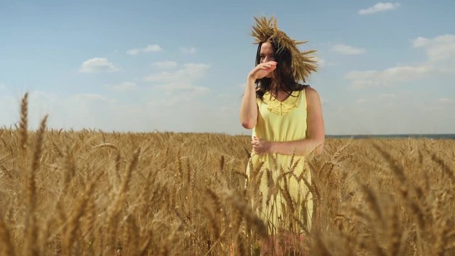 Woman in wheat crown and yellow dress stares into the distance. Summer wheatfield