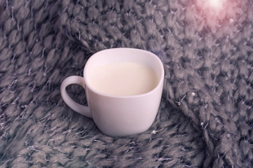 Obraz na płótnie Canvas Milk in a white mug. In the background a gray knitted scarf.