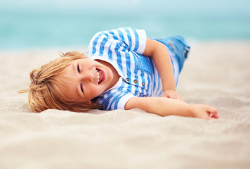 Fototapeta na wymiar cute happy laughing boy, kid having fun on sandy beach, summer vacation