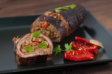 Stuffed meat with parsley and sun-dried tomatoes in olive oil on a black plate