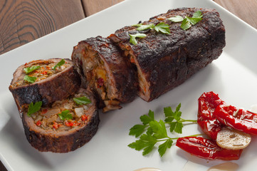 Stuffed meat with parsley and sun-dried tomatoes in olive oil on a black plate
