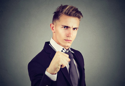 Angry business man with closed fist looking at camera on gray background