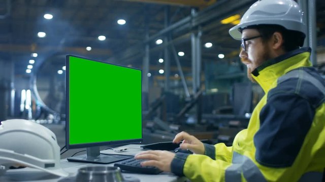 Inside the Heavy Industry Factory Industrial Engineer Works on the Personal Computer with Green Mock-up Screen.