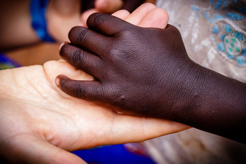 A white girl offering here hand to a black girl during a charity meeting in central Uganda