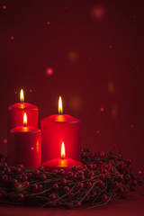 Red burning Advent Christmas candles with the berries wreath on a red background
