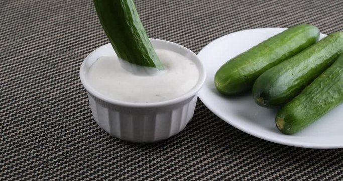 Video of a plate of small bite size cucumbers to the side of a bowl of ranch dressing with one cucumber being skewered with a fork and dipped into the dressing.