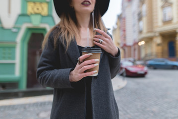 Fototapeta premium A stylish woman holds a cup of coffee or tea in her hands. Hot drink in the hands of a beautiful woman. Hands close-up and in focus.