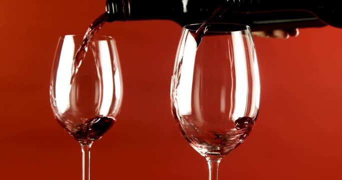 Wine being poured in glasses against red background 