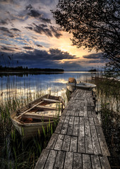 Fototapeta premium małe łodzie na drewnianym molo z zachodem słońca w tle