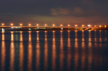 Fototapeta na wymiar Night city embankment in Perm and bridge through the Kama river, lit by lanterns, the reflection of light in water.