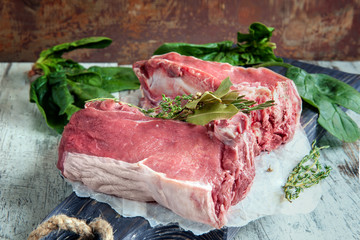 Cuts of beef for grilling on a wooden cutting Board with spinach, rosemary and Provencal herbs for the marinade in a rustic style.