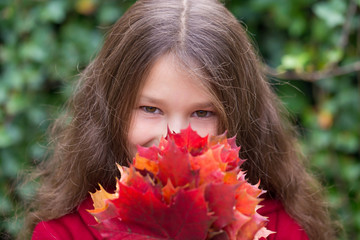 Little girl pre-teen looking out from behind a bouquet of autumn leaves.
