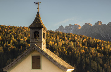 Church tower in front of forest and mountains, Italy