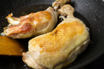 Two roasted chicken legs in black frying pan, close-up view