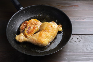 Two roasted chicken legs in black frying pan on dark wooden planks close-up view