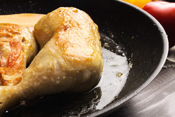 Two roasted chicken legs in black frying pan, close-up view