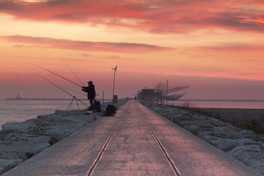 Fishermen at dawn along the pier of Sottomarina, Chioggia, venetian lagoon, Italy