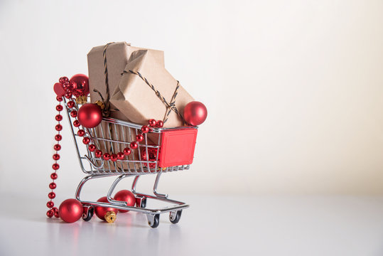 Christmas shopping, gift boxes in kraft paper and red baubles in a shopping cart or trolley on a light background with copy space