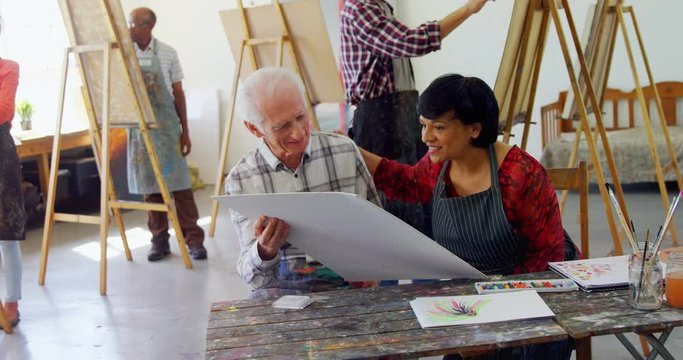 Mixed-race rawing teacher assisting senior man in drawing 