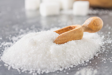 A pile of white sugar sand with a wooden scoop on a dark background.