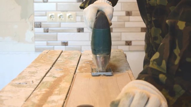 The man cuts the laminate panel with an electric jigsaw.