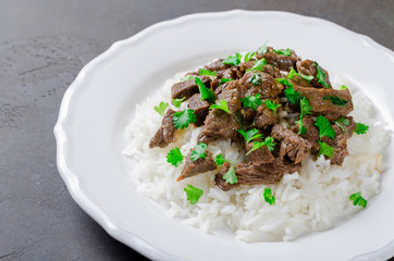 Cooked rice and fried beef with parsley served in white plate on
