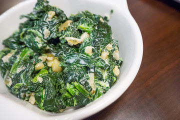 The spinach with garlic butter in white bowl close up image.