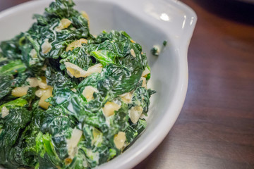 The spinach with garlic butter in white bowl close up image.