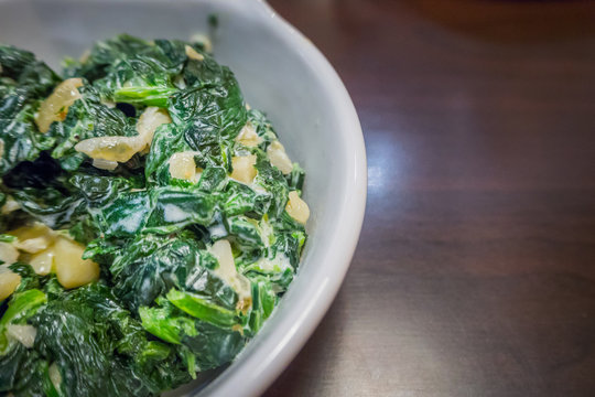 The spinach with garlic butter in white bowl close up image.