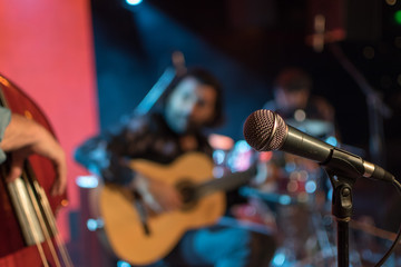 Acoustic trio band performing on a stage in a nightclub, with the microphone in focus waiting for...
