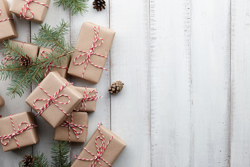 Christmas presents and gift boxes wrapped in kraft paper and fir tree decorations on white wooden background, copy space