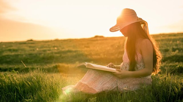 Girl reading the book on rural landscape at sunset