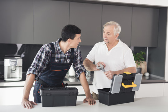 Two men of plumbers stand in the kitchen and choose a tool for working with pipes that are fixed in the apartment.