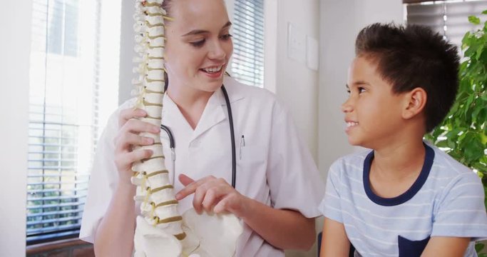 Female physiotherapist explaining spine model to boy patient 