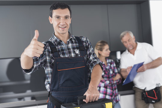 The plumber is posing in the kitchen. He shows his thumb up and smiles.