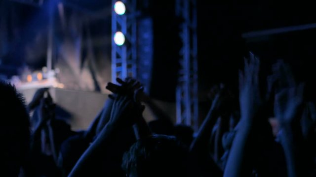 Silhouettes of people partying and clapping at rock concert in front of the stage. Blue stage lighting