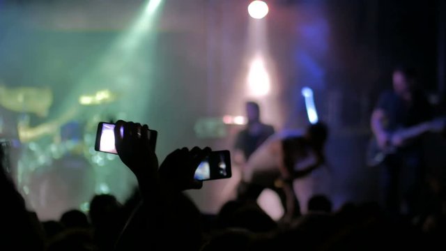 Unrecognizable hands silhouette taking photo or recording video of music concert with smartphone. People partying and clapping in front of the stage. Photography, entertainment and technology concept