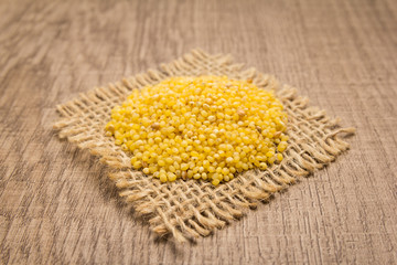 Proso Millet cereal grain. Grains on square cutout of jute. Wooden table. Selective focus.