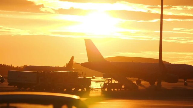 Airplain taxiing at airport ramp and ground support equipment against sunset sky