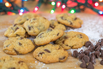 Freshly baked chocolate chip cookies on wooden board with colored lights in background, selective focus