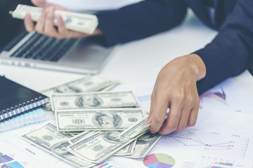 Business concept : Businesswoman counting The United States hundred-dollar bills with business charts , laptop and notebooks on the table