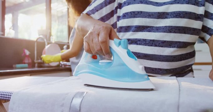 Senior woman ironing clothes in the kitchen  