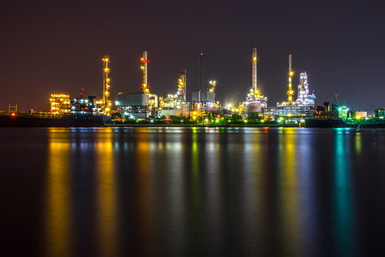 Oil refinery, tanker ship and petrochemical plant at night beside Chao Phaya river, Thailand. Colorful light reflection.