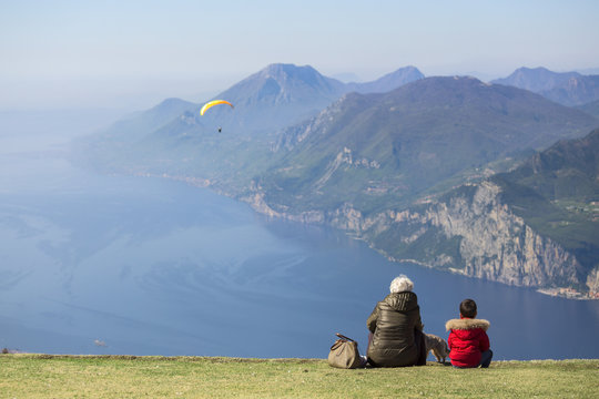 Madam and child look at the paratrooper flying over Garda lake, Baldo mount, Verona, Italy
