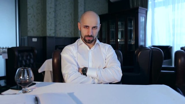 Portrait of a successful serious bald businessman in a restaurant at the table.