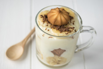 Banana pudding with biscuits and grated chocolate with a wooden spoon on a white table.